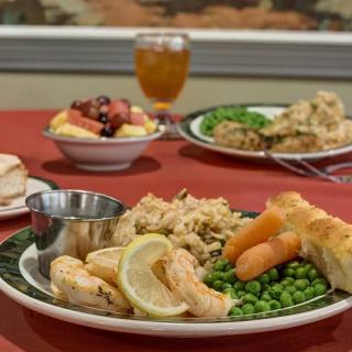 A dinner plate featuring shrimp, rice, carrots, peas, and a bread roll served at a restaurant.