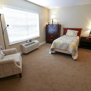 A cozy bedroom with a single bed, armchair, and large window providing natural light.