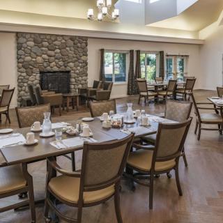 A well-appointed dining room featuring multiple tables and chairs, with a cozy fireplace and windows providing natural light.