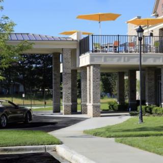 A modern building with a patio featuring bright umbrellas, adjacent to a parked car and surrounded by greenery.