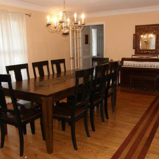 A spacious dining room with a long table surrounded by chairs, featuring a chandelier and wooden flooring.
