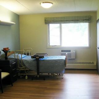 An empty hospital room with a single bed and a window letting in natural light.