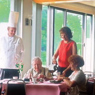 A chef and a waitress serve meals to two customers at a restaurant.