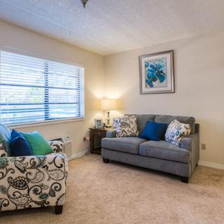 A cozy living room with a gray sofa, patterned armchair, lamp, and wall art.