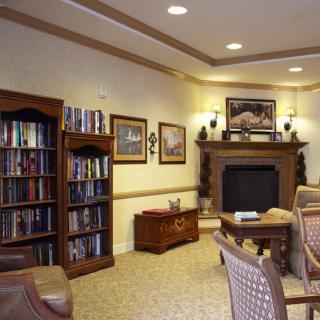 A cozy library room with bookshelves, a fireplace, and comfortable seating.