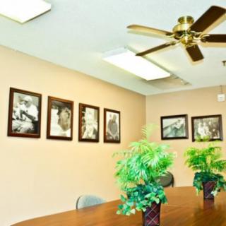 A meeting room with framed artwork on the walls, potted plants on the table, and a ceiling fan overhead.