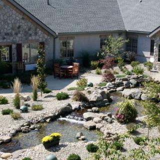 A beautifully landscaped garden with a pond, surrounded by rocks and plants, adjacent to a house.