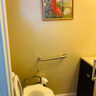 A bathroom with a toilet, grab bar, and sink, decorated with a colorful artwork on the wall.
