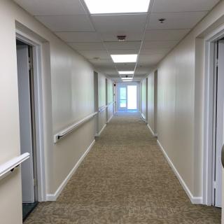 A long indoor hallway with carpet, doors on both sides, and overhead lighting.