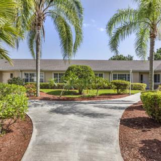 A well-maintained residential building surrounded by landscaped gardens and palm trees on a sunny day.