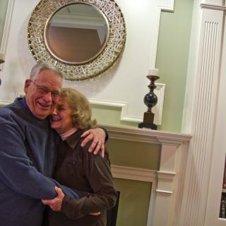 A happy couple embracing in front of a fireplace with decorative items.