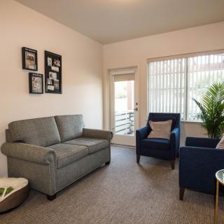 A cozy living room with a gray sofa, two blue armchairs, and a large window.