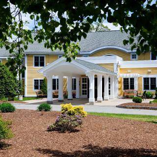 A sunny view of a large yellow house with a welcoming entrance and well-maintained garden.