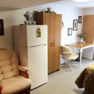 A cozy living area featuring a refrigerator, armchair, and desk with decor.