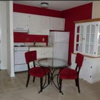 A compact kitchen with a red and white color scheme, featuring a round glass table and two chairs.