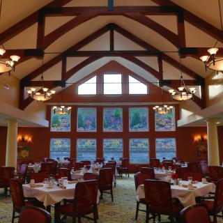 A spacious dining room with high ceilings and large windows, featuring elegantly set tables and chairs.