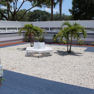 A peaceful garden area with a gravel surface, featuring palm trees and a white bench.