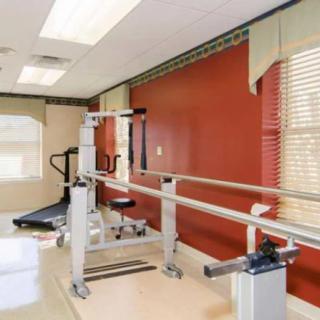 A well-lit therapy room equipped with parallel bars and rehabilitation equipment.