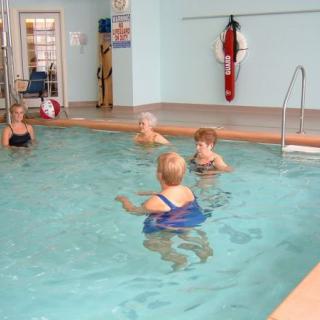 A group of seniors participating in a water aerobics class in an indoor swimming pool.