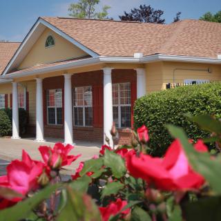 A charming building with white columns, surrounded by vibrant red flowers on a sunny day.