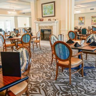 An elegant dining area with neatly arranged tables and chairs, featuring a patterned carpet and a fireplace.