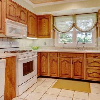 A classic kitchen with wooden cabinets, featuring a stove, oven, and microwave, accented by tiled flooring and a window with curtains.