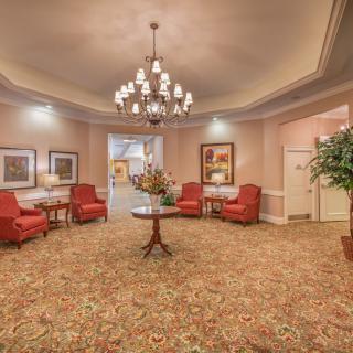 A warmly lit lobby with red upholstered chairs and a central chandelier.