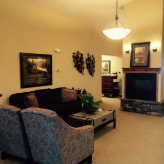 A cozy living room with a sofa, armchair, and fireplace, adorned with artwork and an indoor plant.