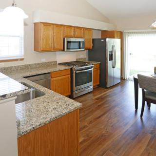A modern kitchen with granite countertops and stainless steel appliances, featuring wood flooring and an adjacent dining area.