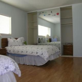 A neatly arranged bedroom with a bed, mirrored closet doors, and wood flooring.