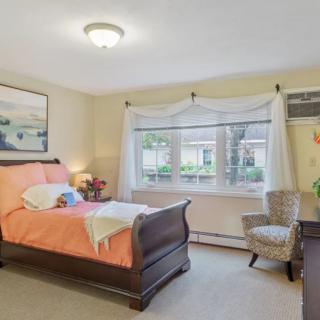 A cozy bedroom with a wooden bed, a chair by the window, and wall decor.