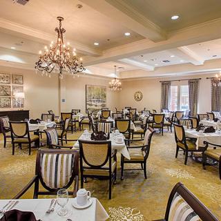 An elegant dining room with neatly arranged tables and chairs, illuminated by chandeliers.
