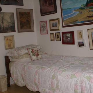 A cozy bedroom with a single bed and walls adorned with various paintings and artwork.