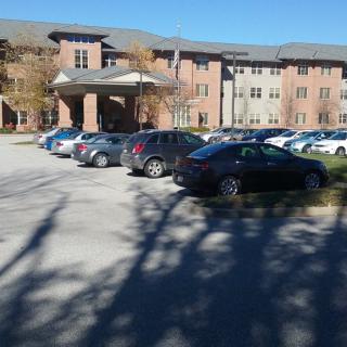 A residential building with a parking lot filled with cars and surrounding trees.
