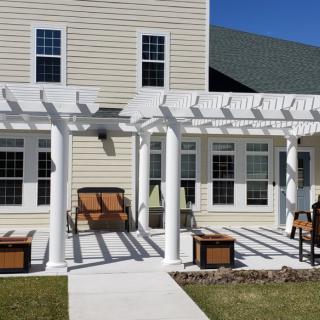 A cozy patio with a white pergola and outdoor seating in the backyard of a house.