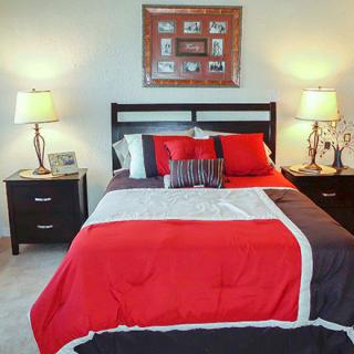 A cozy bedroom featuring a neatly made bed with red and black bedding, flanked by two nightstands with lamps.