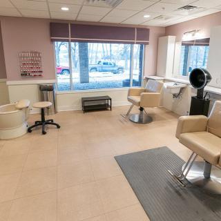 A modern hair salon interior with chairs, mirrors, and a dryer near the window.