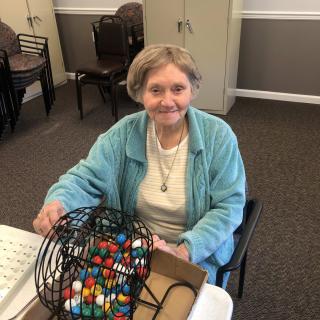 An elderly woman smiling while playing bingo indoors.