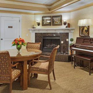 A cozy living room featuring a fireplace, piano, and a dining table with chairs.