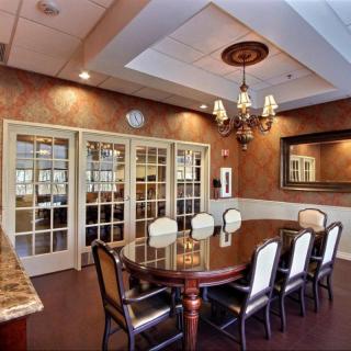 A well-furnished conference room with a large wooden table and elegant chairs, decorated with a chandelier and mirrored wall.