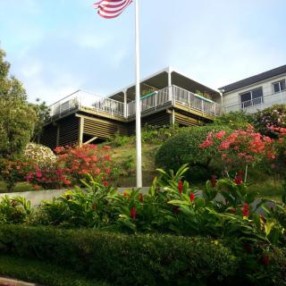A scenic view of a house with a garden, American flag, and elevated patio.