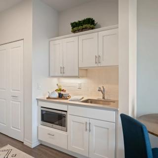 A compact kitchenette with white cabinetry featuring a microwave and sink.
