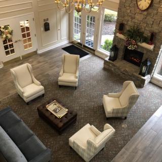 An elegant living room featuring a seating arrangement of white chairs and a couch around a central coffee table, with a stone fireplace and large windows providing ample light.