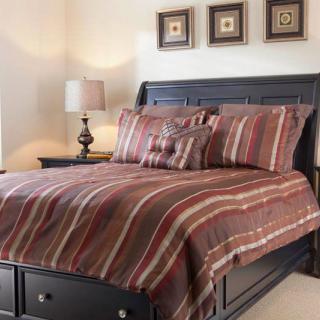 A cozy bedroom featuring a bed with striped bedding, complemented by a nightstand and lamp, decorated with framed artwork on the wall.