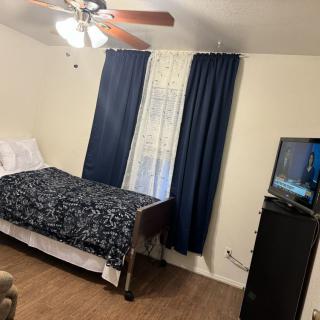A cozy bedroom featuring a single bed, ceiling fan, and television.