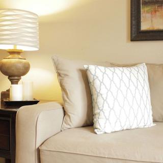 A cozy living room with a beige couch and a patterned pillow, accompanied by a stylish lamp on the side table.