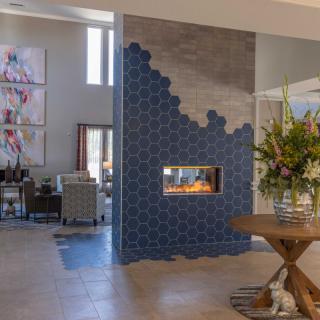 A modern living room with a stylish fireplace surrounded by blue tiles and decorated with artwork and a flower arrangement.