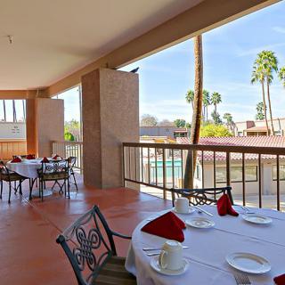 An outdoor dining area with tables set elegantly, overlooking a pool and palm trees.