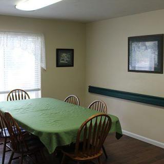 A cozy dining room with a green tablecloth on the table and artwork on the walls.