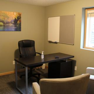 A tidy office with a desk, chairs, and a painting on the wall.
